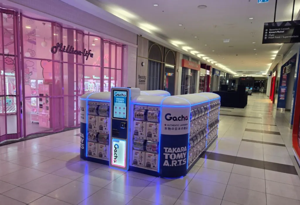 White Gacha capsule kiosk with a glowing blue canopy in the mall walkway at Northland Shopping Centre