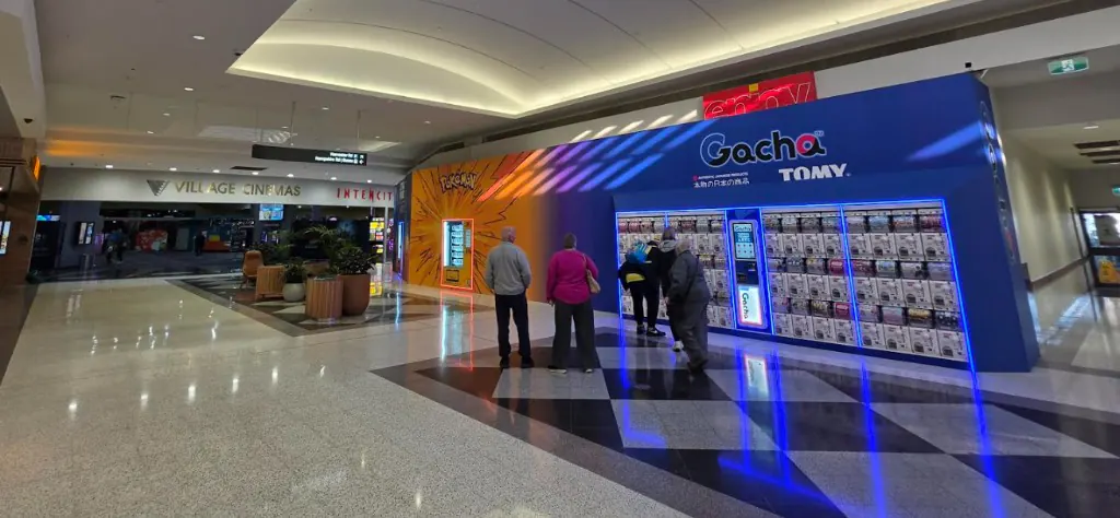 Dedicated Gacha wall inside Sunshine Marketplace, with rows of capsule machines under the illuminated Gacha sign